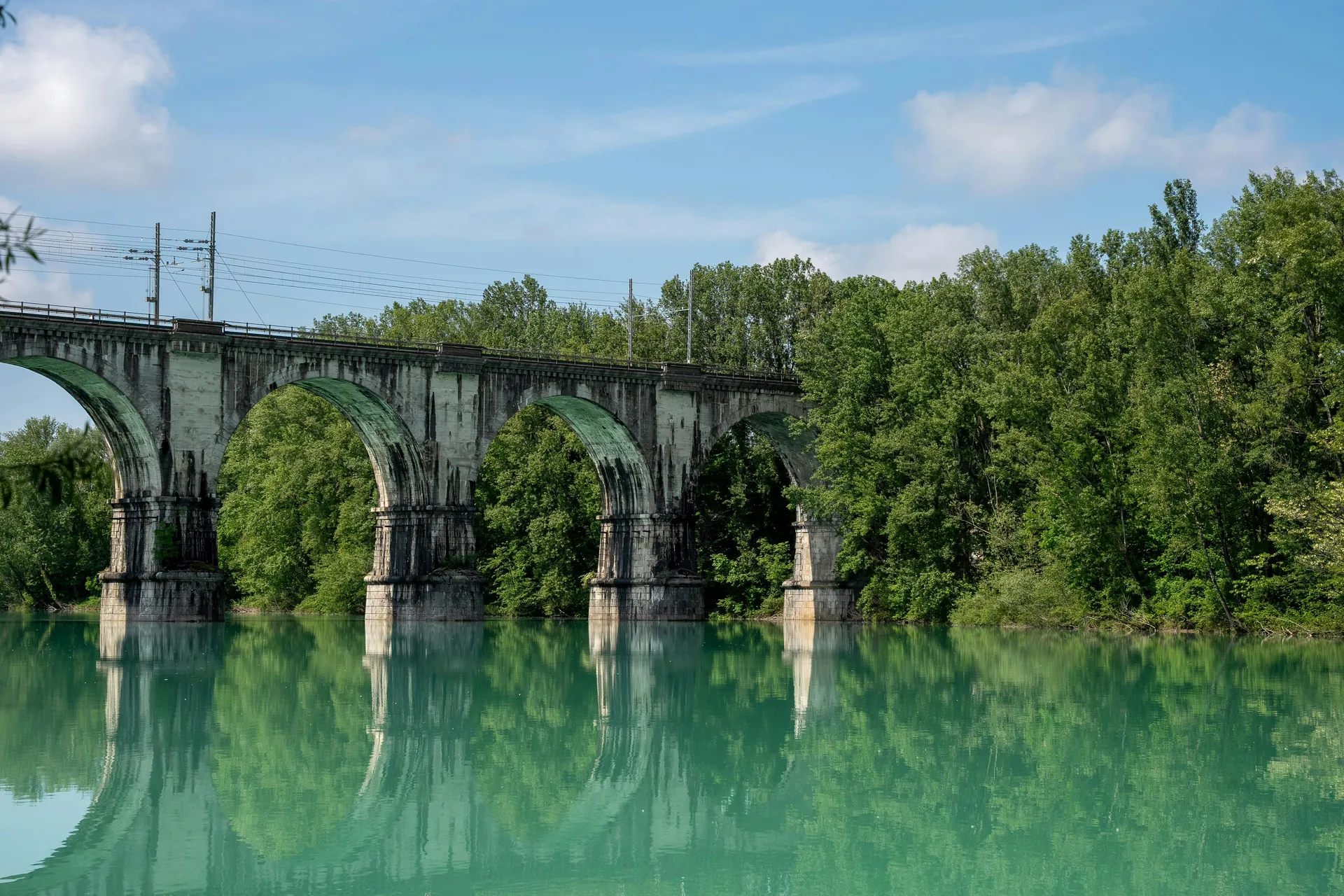 Beautiful arched railway bridge spanning across a serene river in Gorica, Radovljica, Slovenia, surrounded by lush greenery.