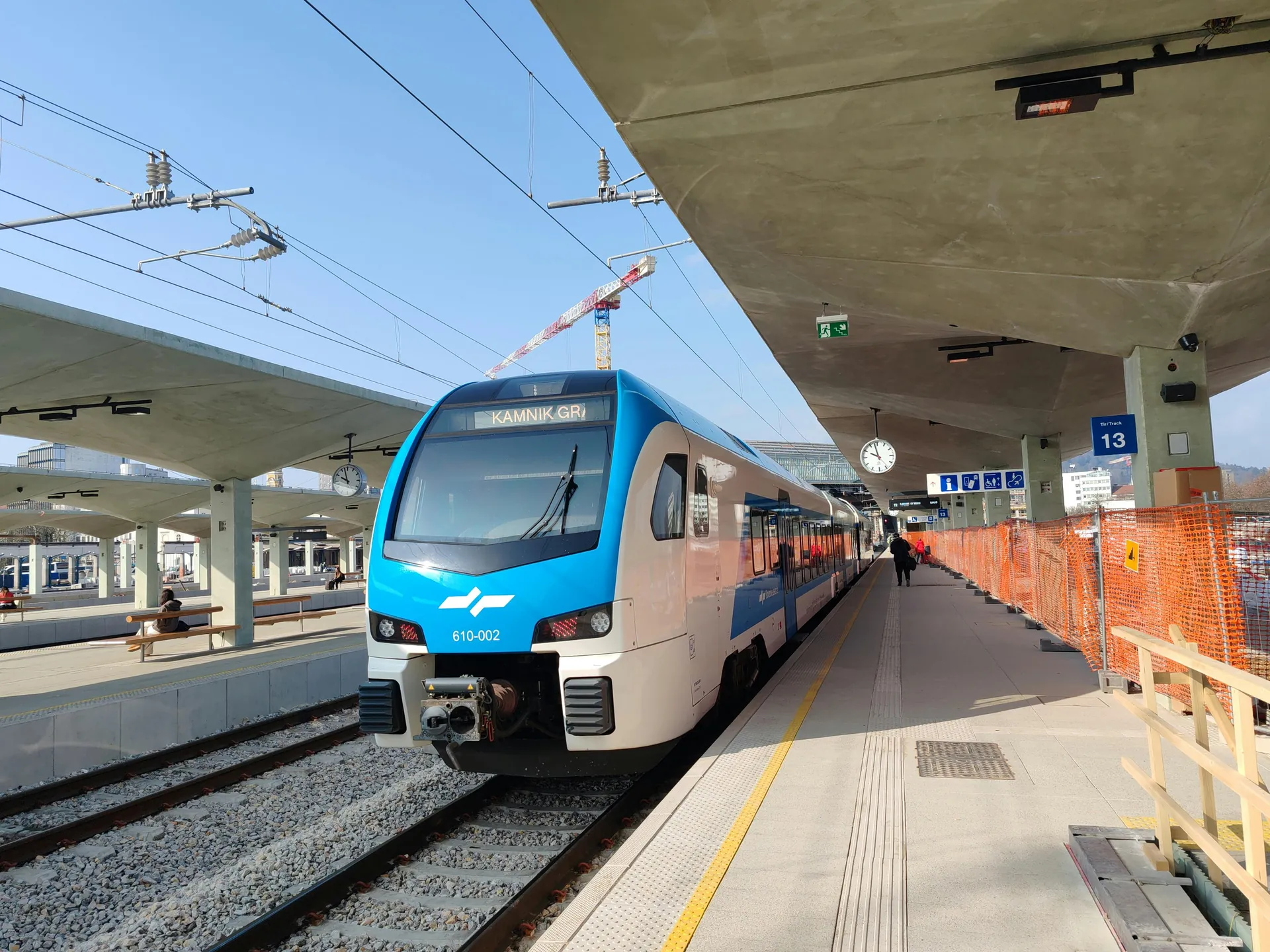 A sleek blue and white train at Ljubljana station under a clear blue sky.